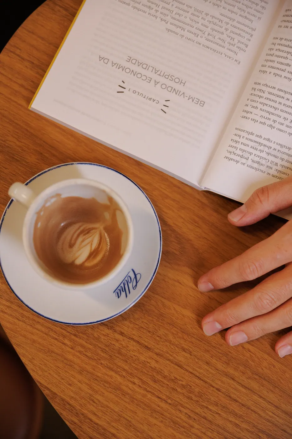 Xícara de café da Colha ao lado de um livro sobre mesa de madeira