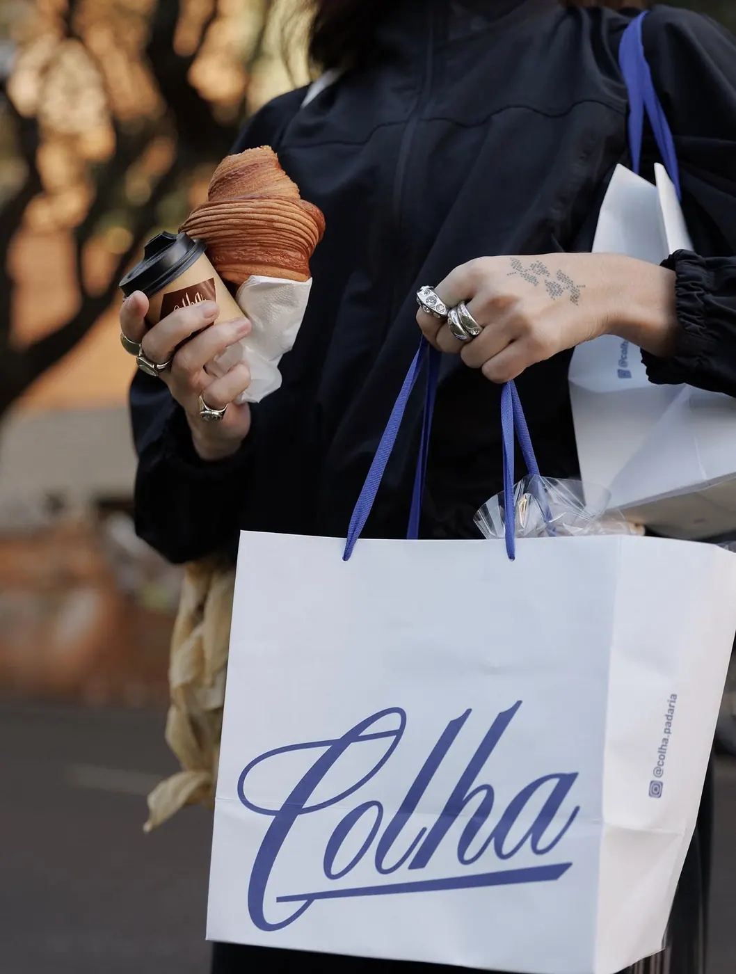Cliente com café, croissant e sacola azul da Colha