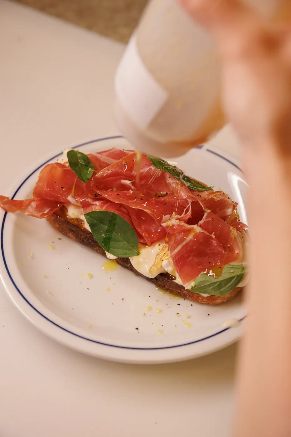 Tartine de presunto parma, stracciatella e manjericão em prato azul