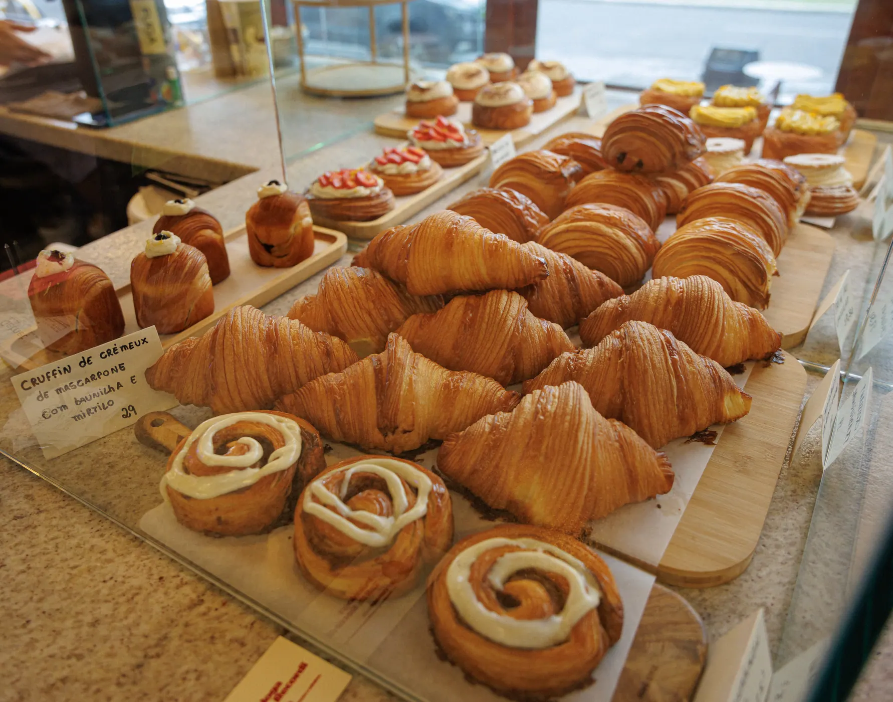 Vitrine da Colha com croissants, cinnamon rolls e danishes expostos em tábuas de madeira